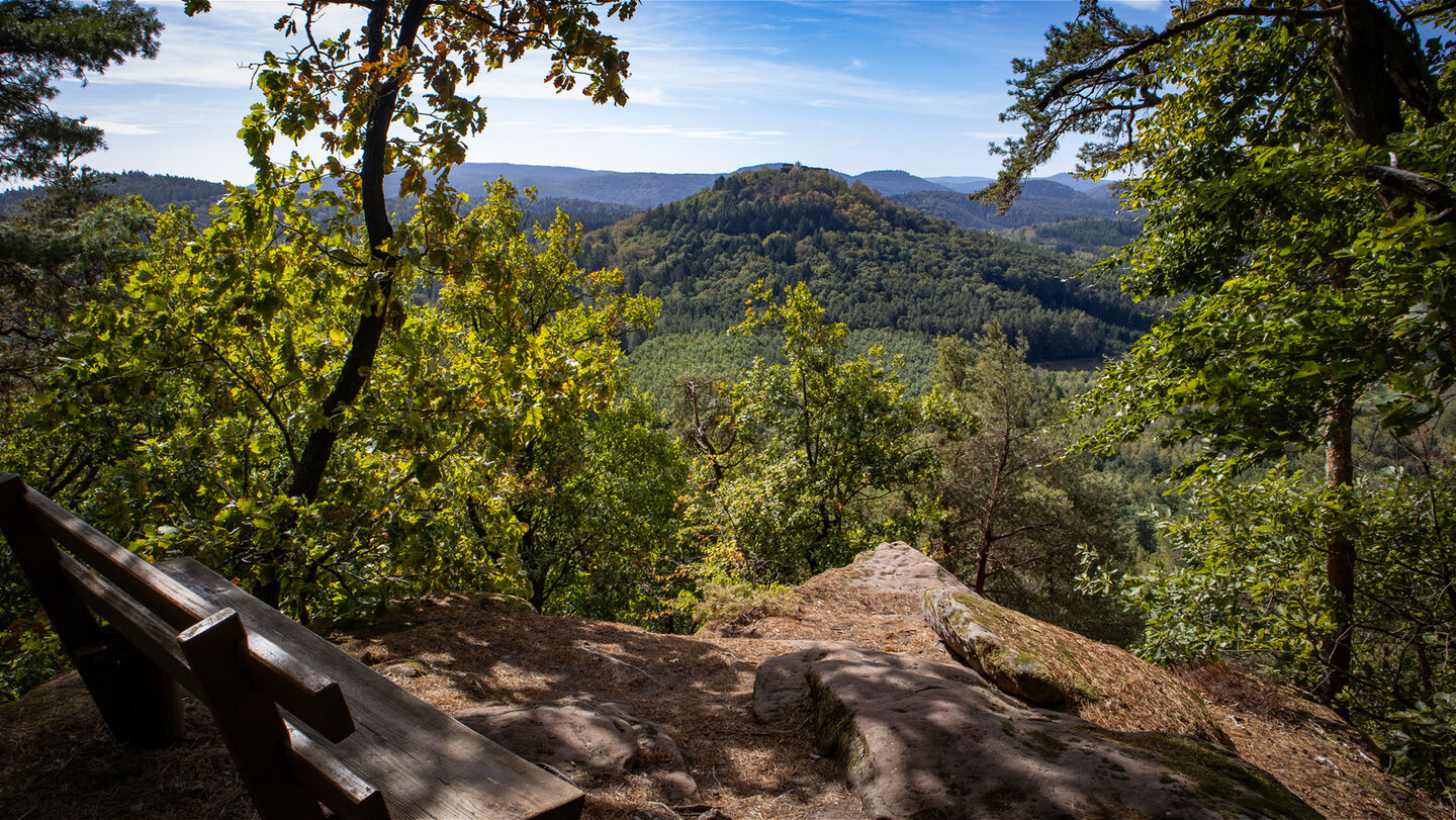 Holzbank auf einem Buntsandsteinplateau am Immersberg mit Blick über bewaldete Hügel zur Burgruine Lindelbrunn auf einer Bergkuppe