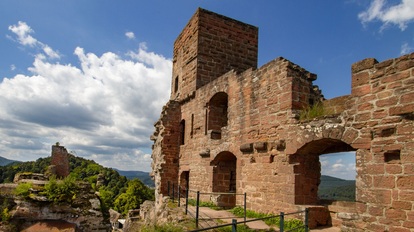 Massive Buntsandstein-Mauerreste mit Torbögen und Turm der Dahner Burgengruppe, im Hintergrund die Ruine Tanstein auf dem Felskamm