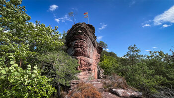 Geschichteter, rötlicher Felsturm am Nedigfelsen bei Hauenstein mit Heidekraut am Fuß und kleiner Kiefer auf der Kuppe