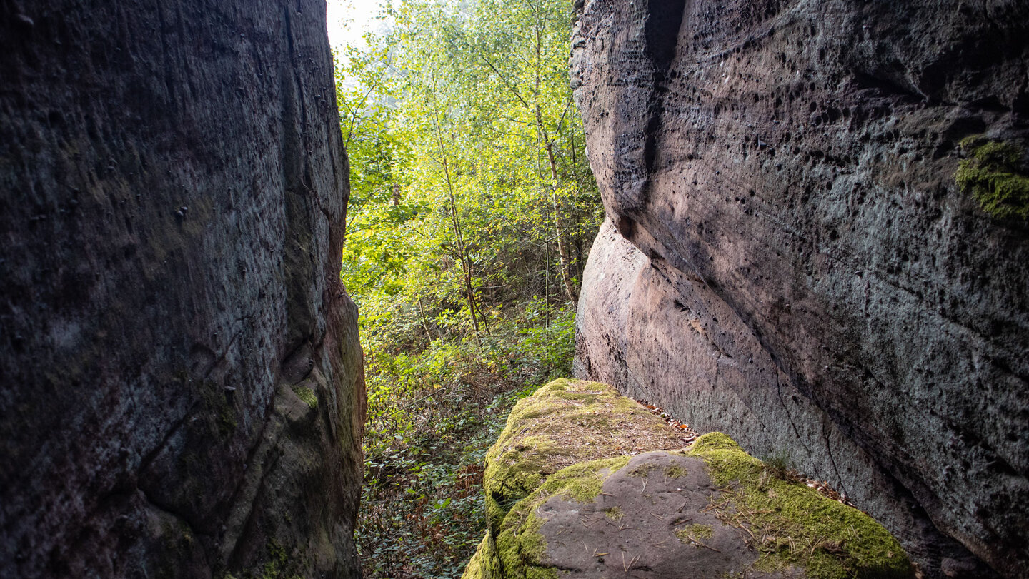 Blick durch die enge Kluft des Großen Zimmerbergfelsens, raue Sandsteinwände zu beiden Seiten, Moos auf dem Felsblock im Vordergrund