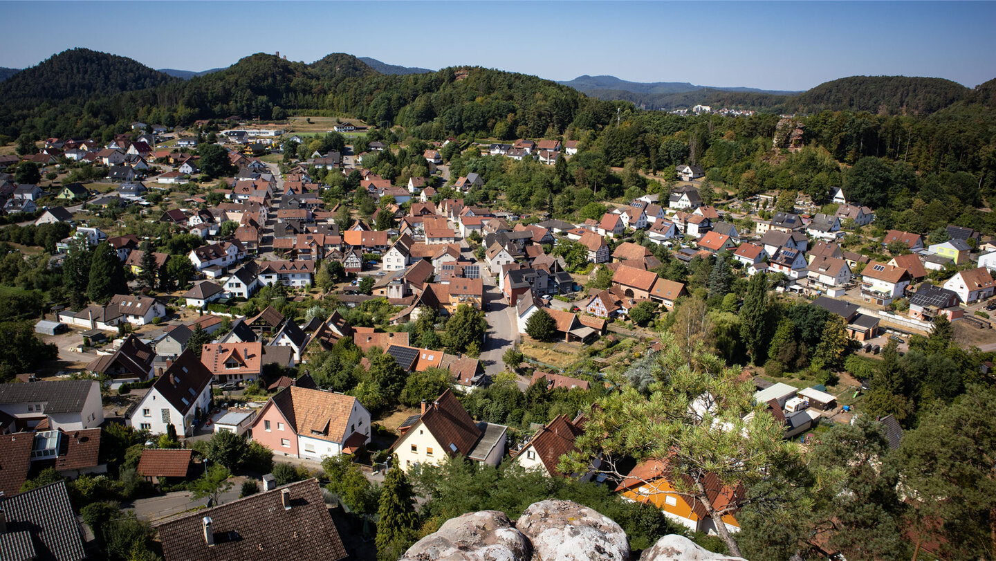 Panoramablick von der Aussichtsplattform des Hahnfels über die Dächer von Erfweiler, im Hintergrund die Burgengruppe Altdahn und bewaldete Höhenzüge