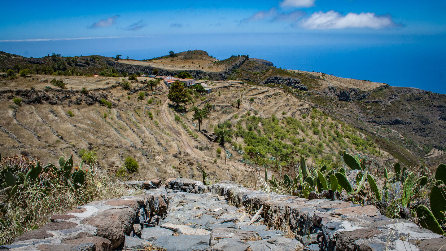 Gepflasterter Wanderweg zum Drago de Agalán bei Alajeró, umgeben von Terrassenfeldern und Meerblick.