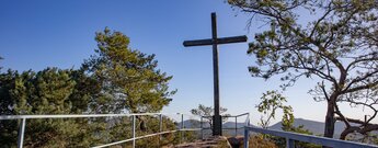 Gipfelkreuz auf der gesicherten Aussichtsplattform des Schweinsfelsens bei Silz mit Geländer, Kiefern und weitem Panorama über das Trifelsland