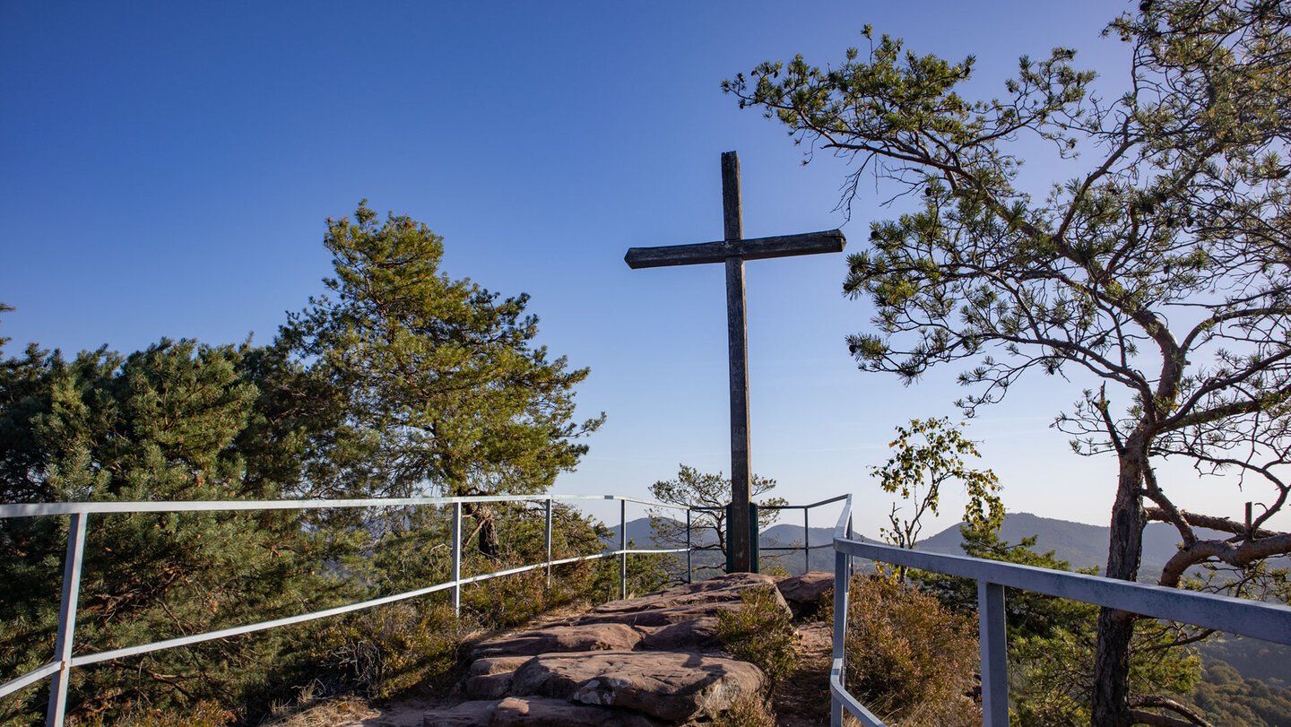Gipfelkreuz auf der gesicherten Aussichtsplattform des Schweinsfelsens bei Silz mit Geländer, Kiefern und weitem Panorama über das Trifelsland