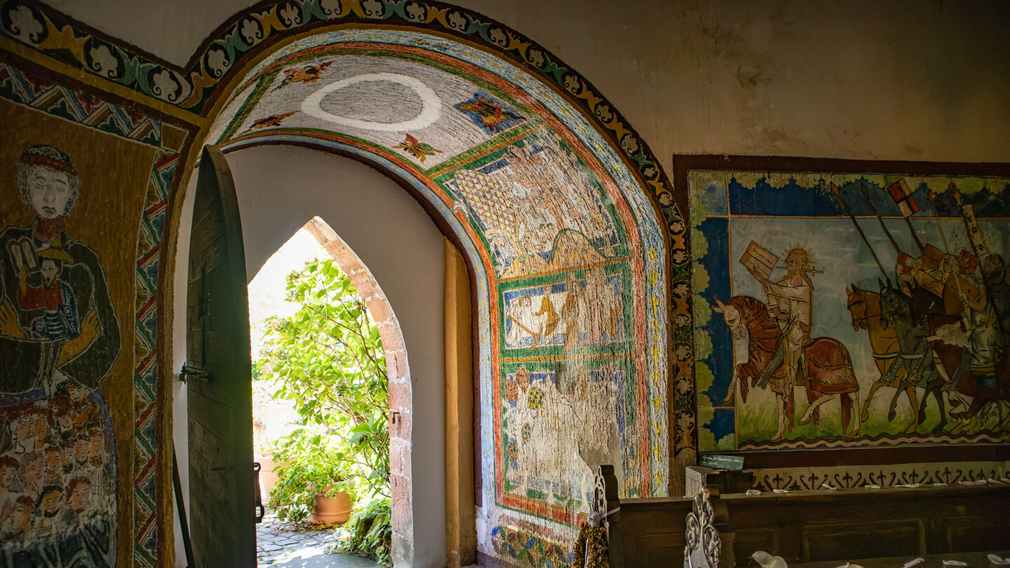 Innenraum der Burgkapelle Berwartstein mit farbigen Wandmalereien, Rundbogenportal und Blick in den Burghof