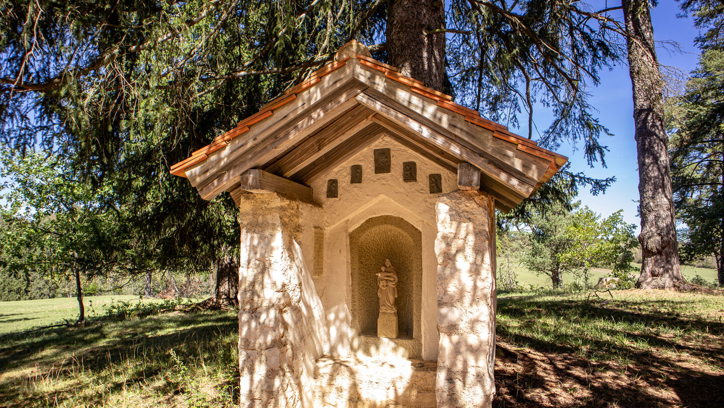 Steinerner Bildstock mit Nische und Heiligenfigur im Wald am Wegesrand