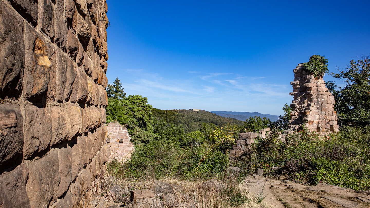 Sandsteinmauer der Drei Egsen mit Blick auf bewaldete Hügel und die Hohlandsbourg am Horizont
