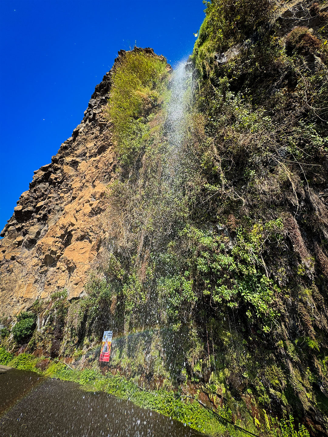 das Wasser des Cascata dos Anjos auf Madeira fällt auf die Straße und bildet Regenbögen