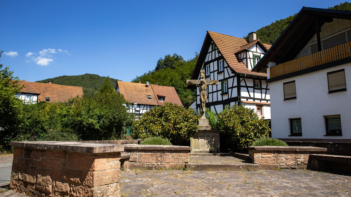 Fachwerkhäuser und steinernes Wegekreuz an einem kleinen Platz in Erfweiler im Dahner Felsenland