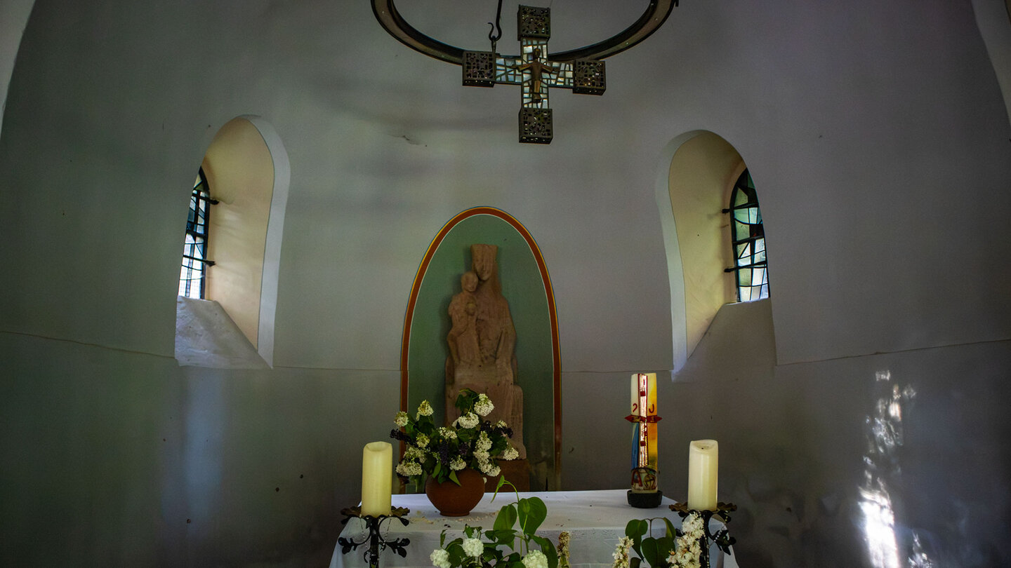 Innenraum des Winterkirchels – Sandsteinfigur der Madonna mit Kind auf dem Altar, flankiert von Kerzen und bunten Glasfenstern