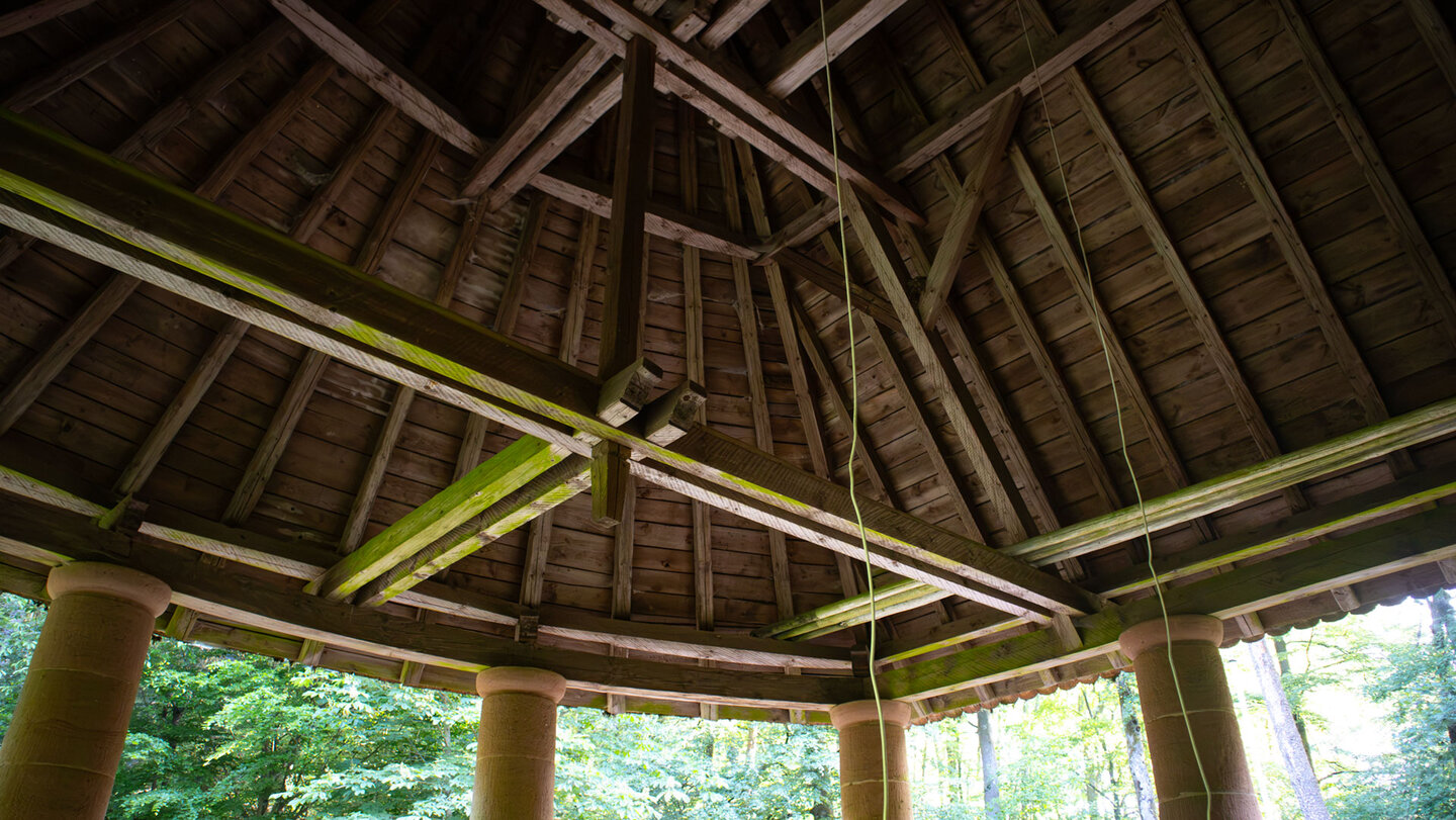 Konstruktion aus Holzbalken unter dem Dach der Waldkapelle mit Seil zum Läuten der Kapellenglocke, Blick durch die Säulen ins Grüne