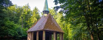 Das Winterkirchel – offene Waldkapelle mit Rundgang aus Sandsteinsäulen, Ziegeldach und kupfernem Turmhelm, umgeben von Laubbäumen