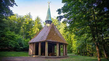 Das Winterkirchel – offene Waldkapelle mit Rundgang aus Sandsteinsäulen, Ziegeldach und kupfernem Turmhelm, umgeben von Laubbäumen