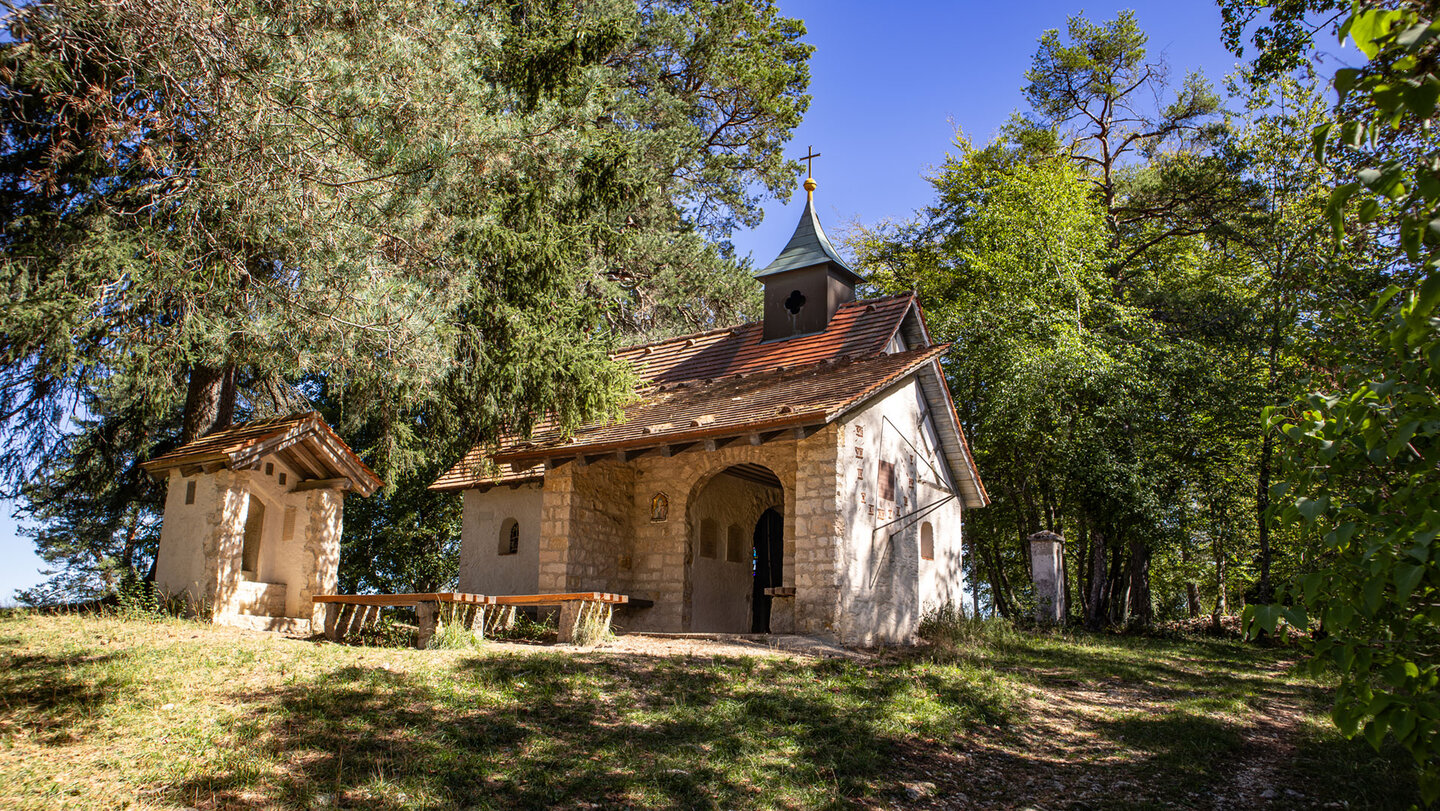 Kleine verputzte Kapelle mit Glockenturm und Kreuz im Wald des Donautals.