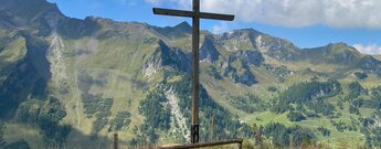 hölzernes Kreuz mit Rappastein und Plasteikopf im Hintergrund