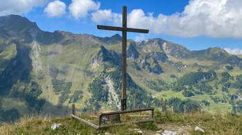 hölzernes Kreuz mit Rappastein und Plasteikopf im Hintergrund