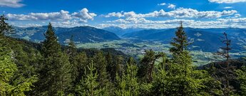 Blick über Saalfelden und das Saalachtal von einer hölzernen Rundbank am Wanderweg