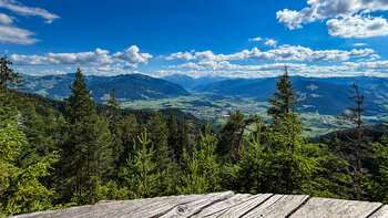 Blick über Saalfelden und das Saalachtal von einer hölzernen Rundbank am Wanderweg
