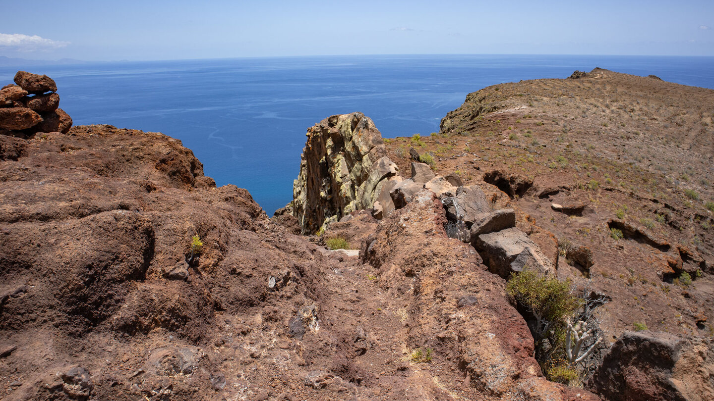 Wanderweg entlang des rötlich gefärbten Bergrückens oberhalb der Playa El Cabrito