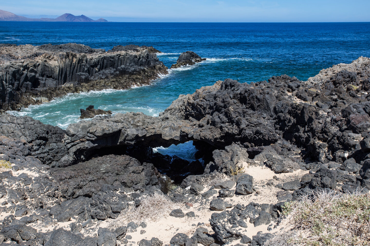 Felsbogen in einer Basaltbucht mit der Insel Alegranza im Hintergrund