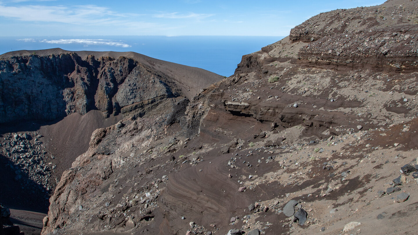 Blick in den Krater Hoyo Negro entlang der zerklüfteten Gesteinsschichten und dem Atlantik im Hintergrund