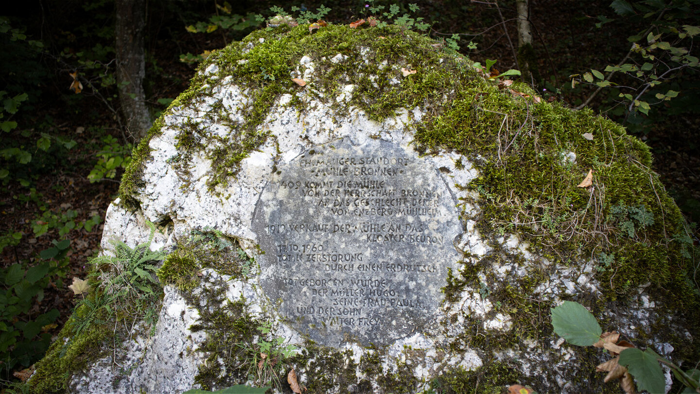 Großer, moosbedeckter Gedenkstein mit eingravierter Inschrift zur Geschichte der Bronner Mühle im Wald