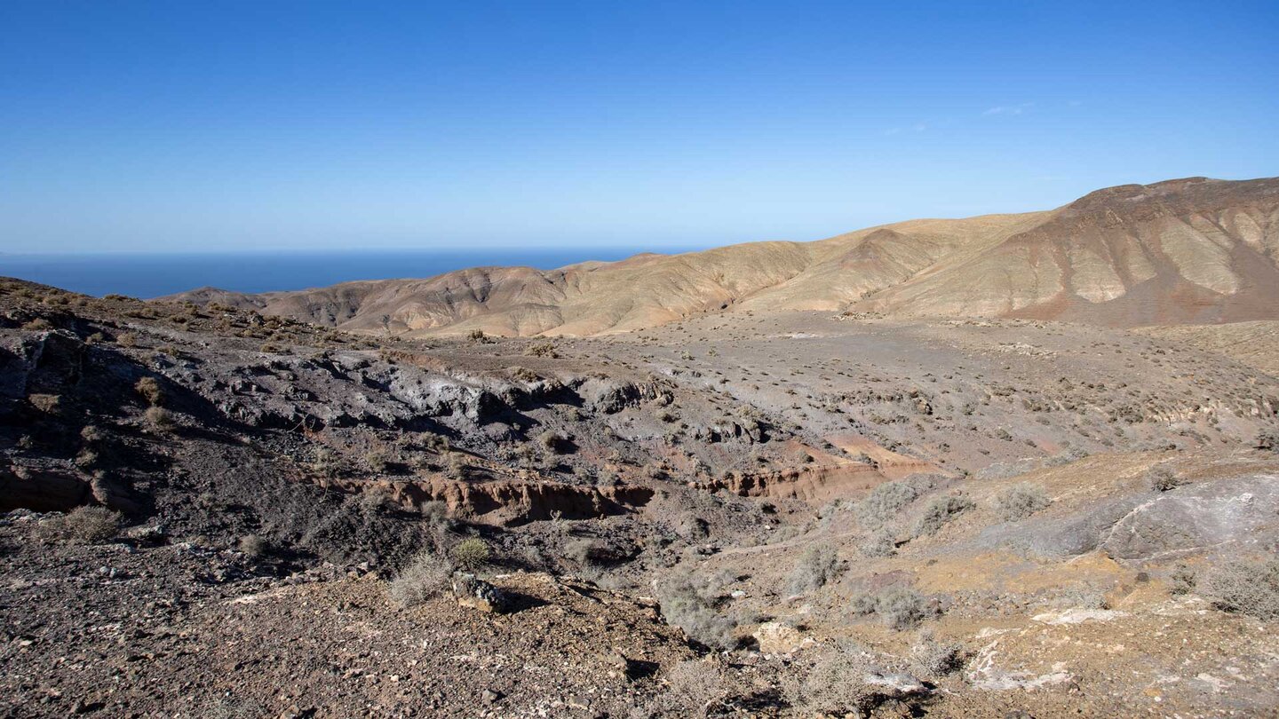 vom Wanderweg blickt man über bunte Erosionsschluchten zur Westküste Fuerteventuras