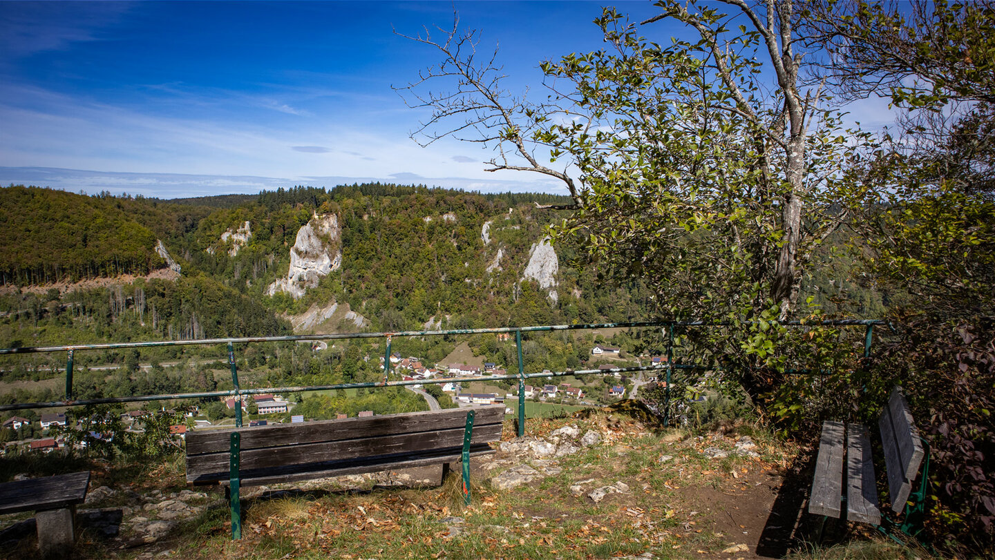 Aussichtspunkt Schlossfelsen mit Holzbänken und grünem Geländer, Blick auf Felsen, Wald und Dorf im Oberen Donautal